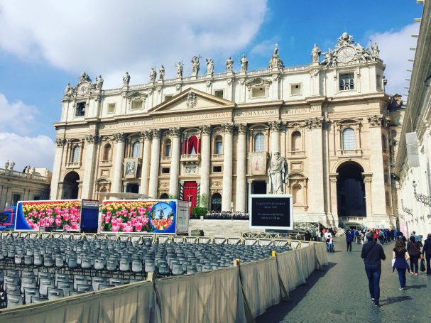 St. Peter's Basilica with red banners, surrounded by empty seats and blue skies.