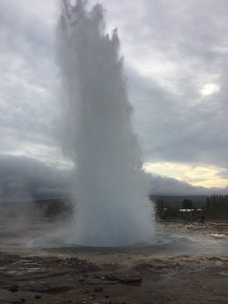 A powerful geyser erupting against a cloudy sky.