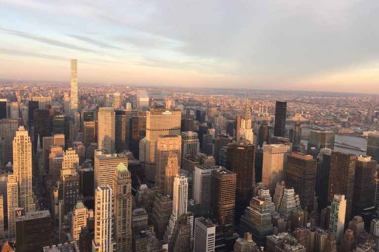 A panoramic view of a city skyline at sunset, showcasing tall buildings and a vibrant horizon.