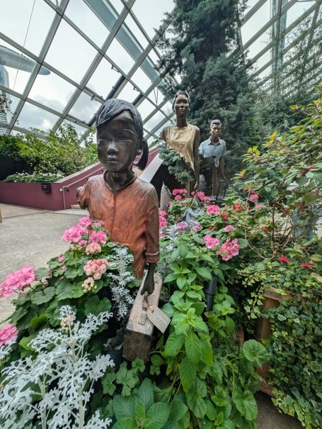 Statues of children surrounded by vibrant flowers in a botanical setting.