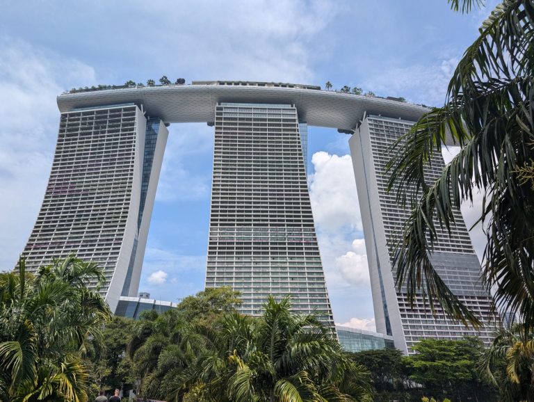 Modern skyscraper with unique design, surrounded by greenery and a bright sky.