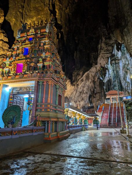 Colourful Hindu temple within a large cave, illuminated by artificial lights.