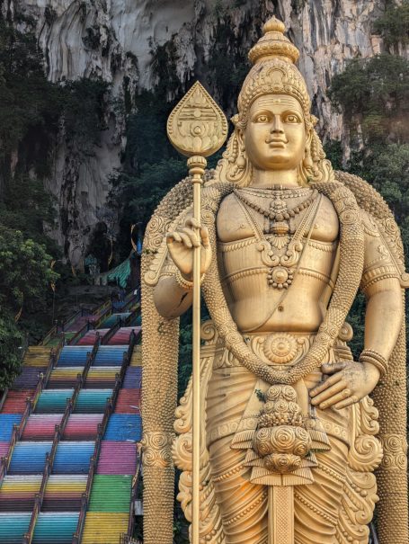 Golden statue of a deity in front of colourful, stepped pathways in a scenic outdoor setting.