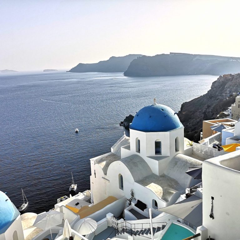 Santorini's white buildings with a blue dome overlooking a calm sea and distant cliffs.