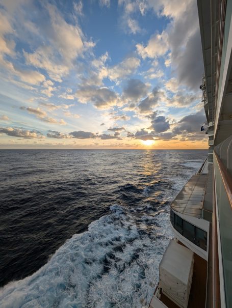 Scenic sunset over the ocean viewed from a ship, with gentle waves and clouds.