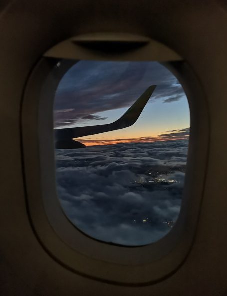 View from an aircraft window, showcasing clouds and a wing against a sunset sky.