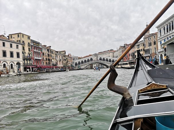 View from a gondola on the Grand Canal, with buildings and a bridge in the background.