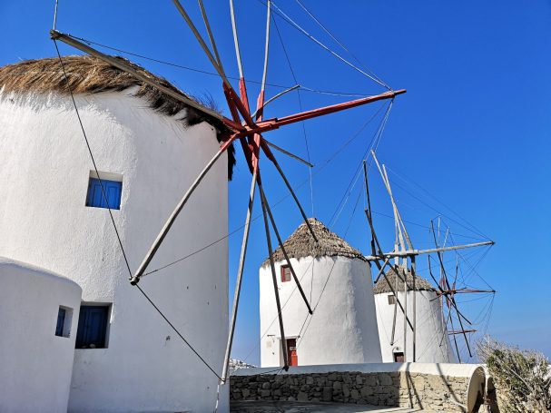 Three traditional windmills with thatched roofs against a clear blue sky.