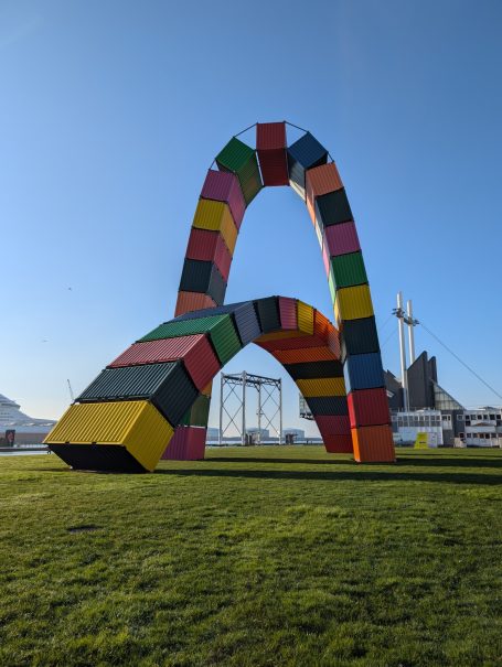 Colourful arch sculpture made of large blocks, set on green grass against a blue sky.