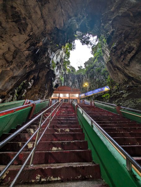 View of steep steps leading to a temple inside a large cave with greenery above.