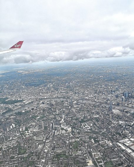 Aerial view of London cityscape with clouds and Virgin airplane wing in the foreground