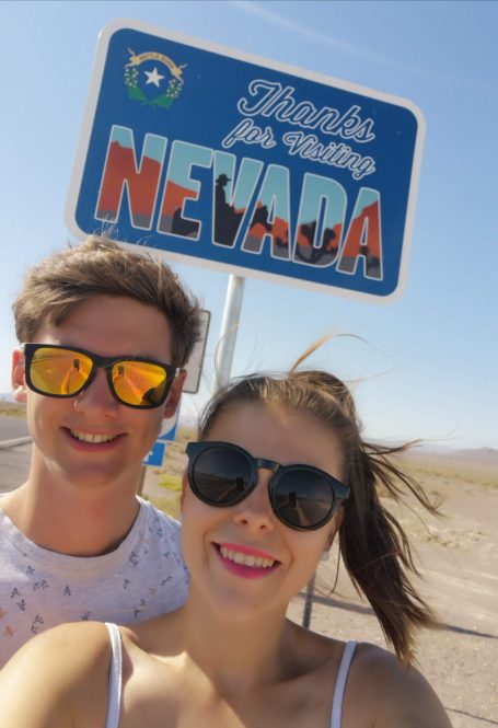 I&B's Founder & Husband posing in front of a "thank you for visiting Nevada" sign, with desert views in the background