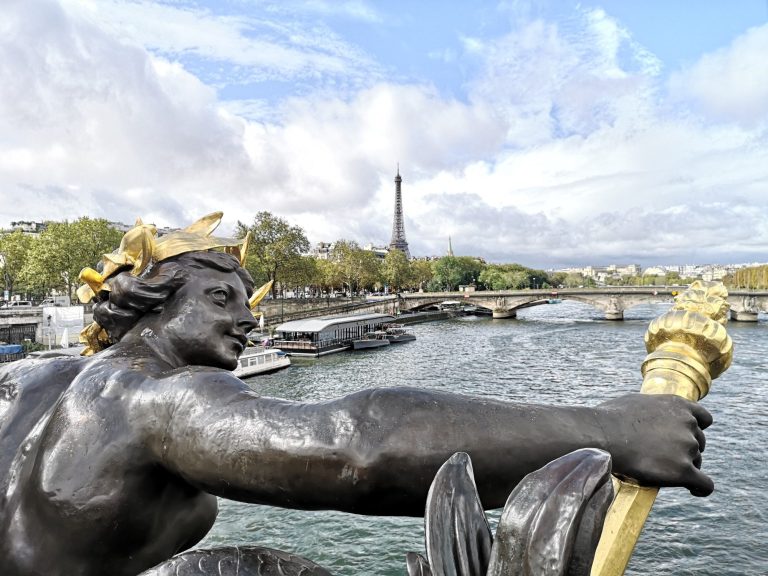 Statue with a torch overlooking the Seine River, with the Eiffel Tower in the background.