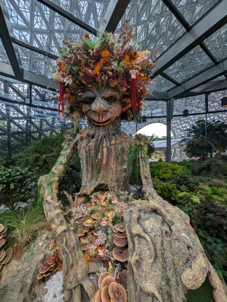 A large tree figure adorned with flowers and foliage in a green garden setting.