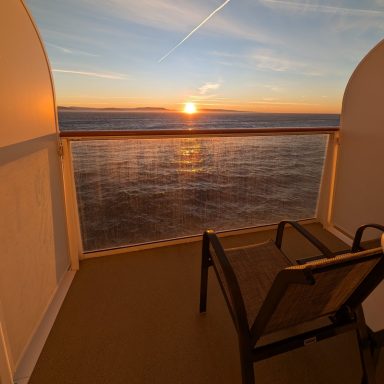 Sunset over the ocean viewed from a balcony with a chair.