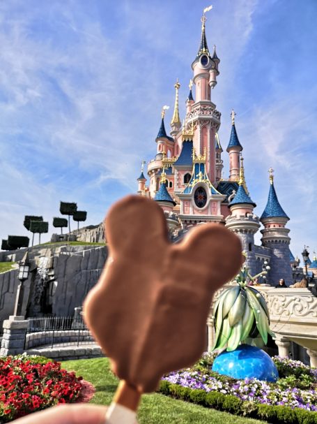 A chocolate-covered ice cream treat in front of a fairy-tale castle at Disneyland.